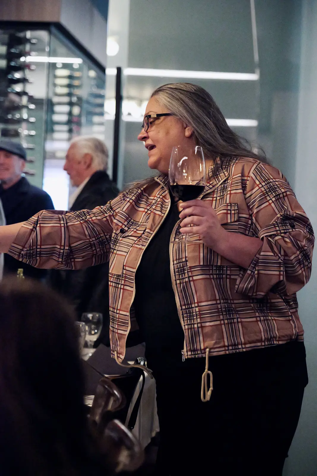 Guest in a plaid jacket greeting someone with a glass of wine