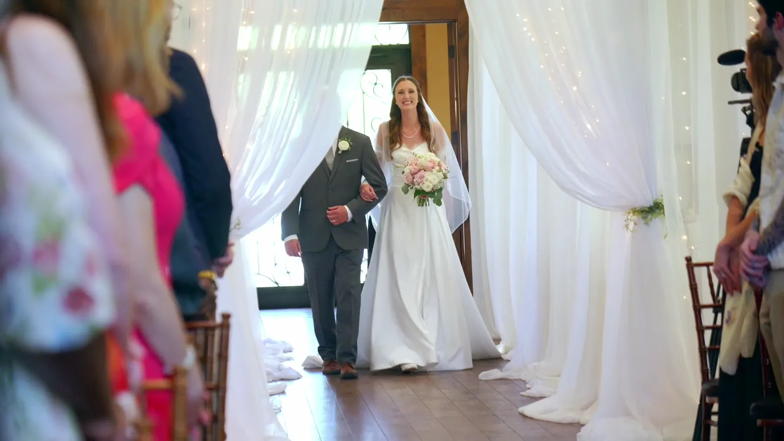 Bride walking down the aisle with her father between white curtains